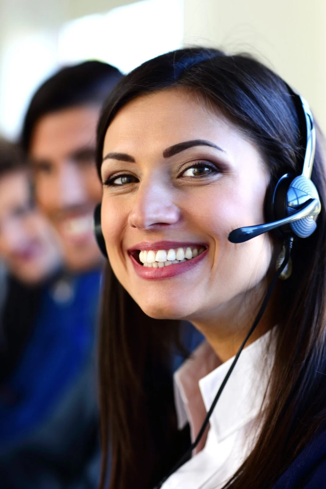 Smiling customer service agent with a headset, her teammates behind her